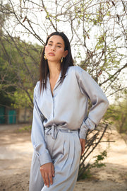 Woman in a light gray outfit standing outdoors with trees in the background